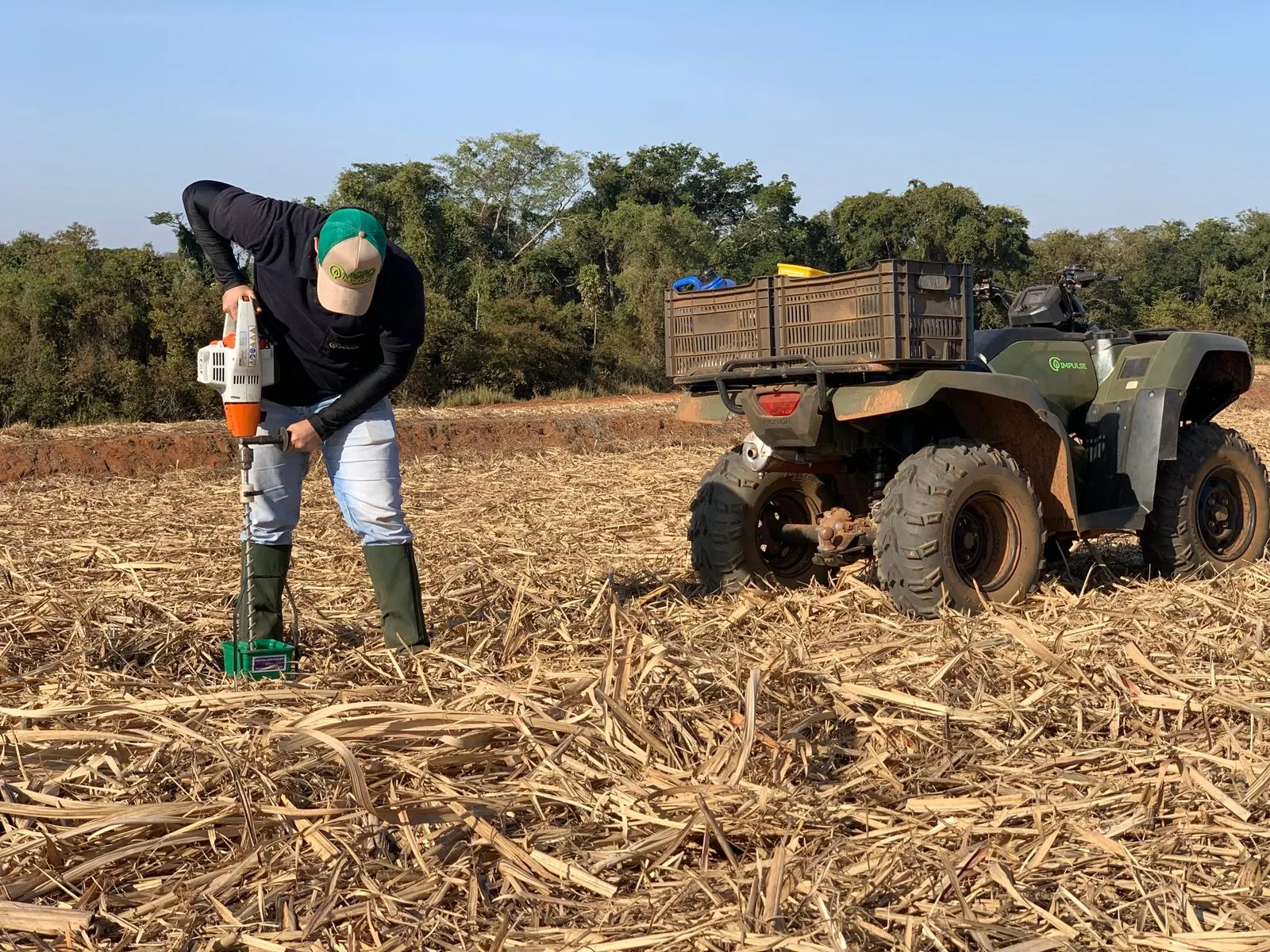 Técnico coletando solo com trado motorizado ao lado do quadriciclo